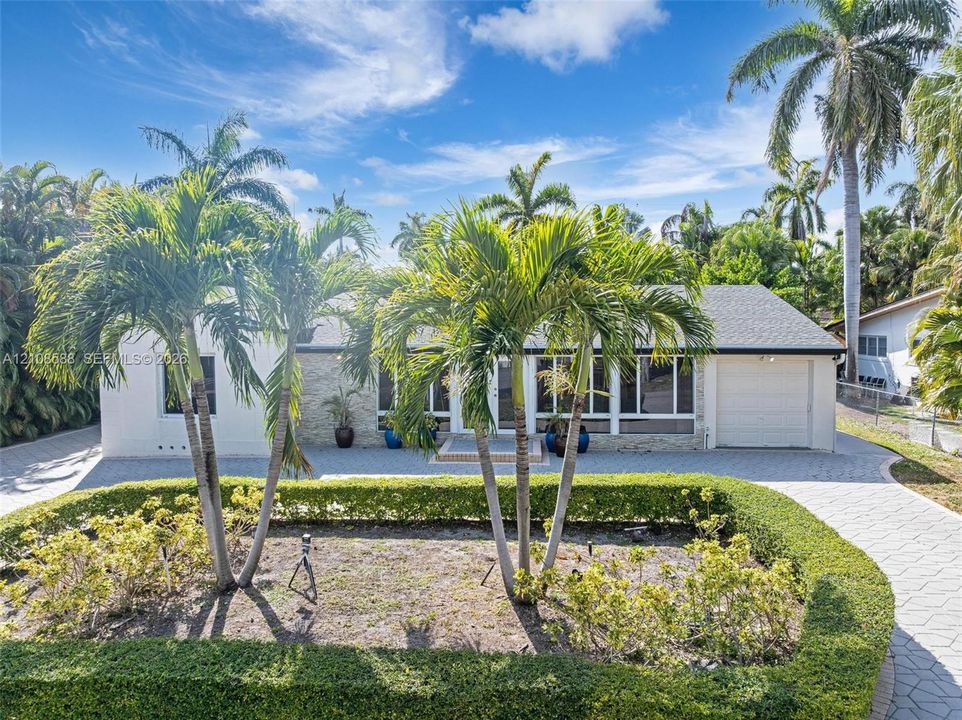 Single-story residence featuring a paved driveway, exterior stone veneer accents, multi-pane windows, attached garage, and mature landscaping with palm trees