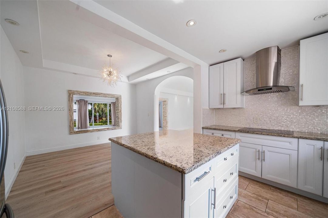 Kitchen featuring white cabinetry, stone-surfaced center island, stainless steel chimney-style range hood, recessed lighting, and wood-finish flooring