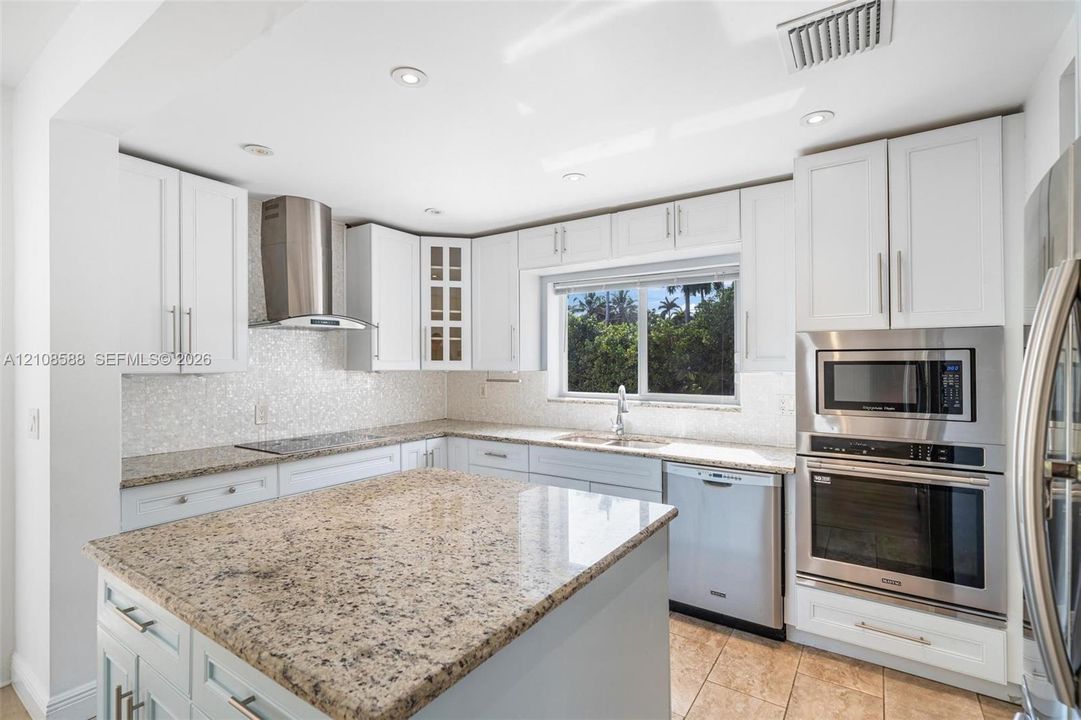 Kitchen featuring white cabinetry, stone countertops, stainless steel appliances including a built-in oven and microwave, mosaic tile backsplash, and a central island