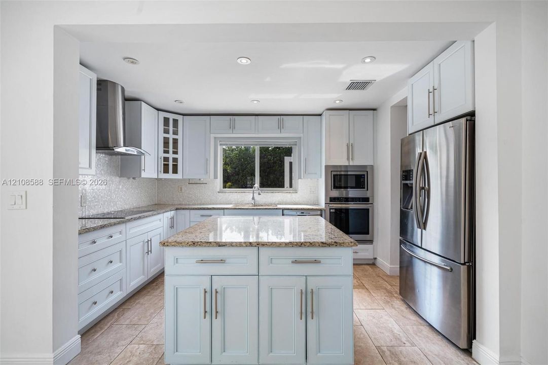 Kitchen featuring white shaker cabinetry, central island with stone countertop, stainless steel appliances, mosaic tile backsplash, and ceramic tile flooring