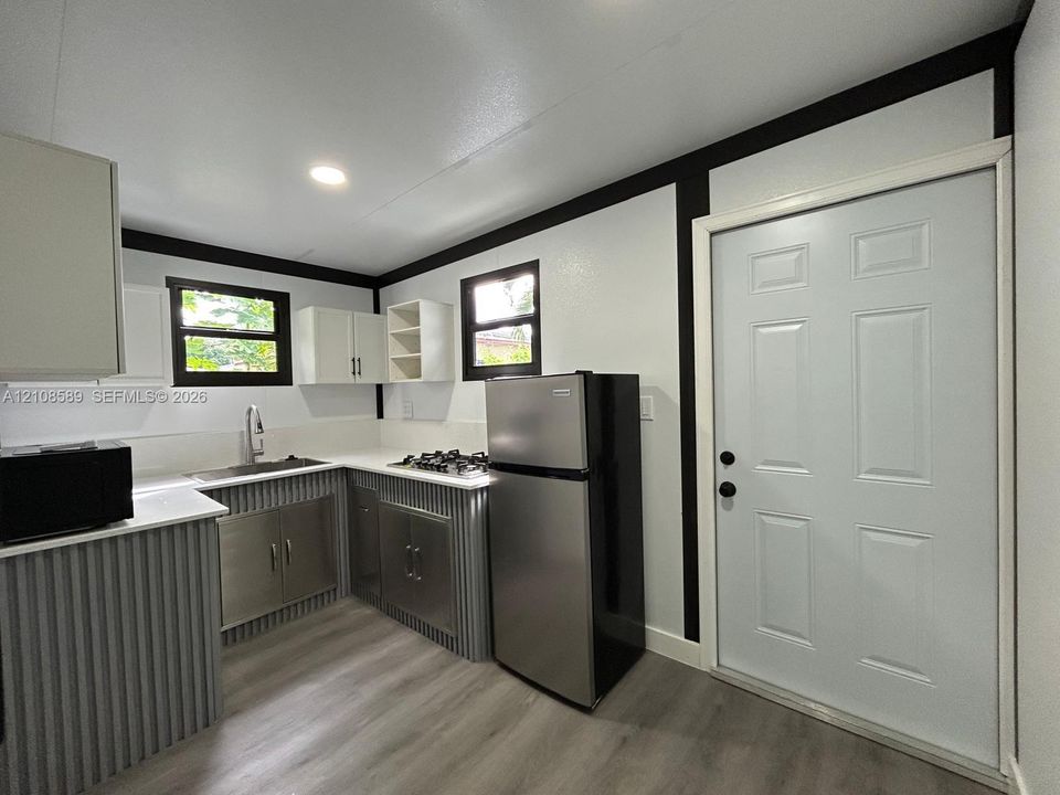 Kitchen featuring metal corrugated cabinetry, white solid-surface countertops, wood-finish flooring, and recessed ceiling lighting