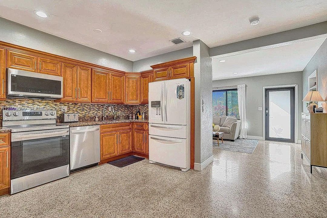 Kitchen featuring wood cabinetry, stainless steel appliances, decorative stone-patterned backsplash, and polished hard-surface flooring with recessed lighting
