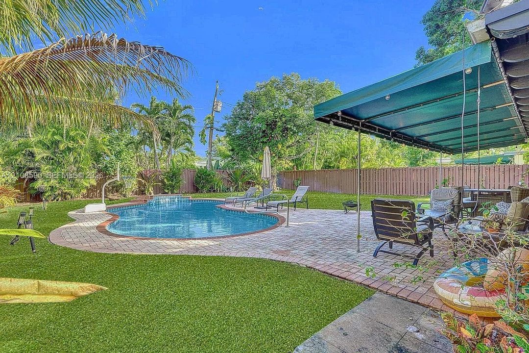 Backyard featuring a swimming pool, expansive paver patio, retractable fabric awning, and perimeter privacy fencing