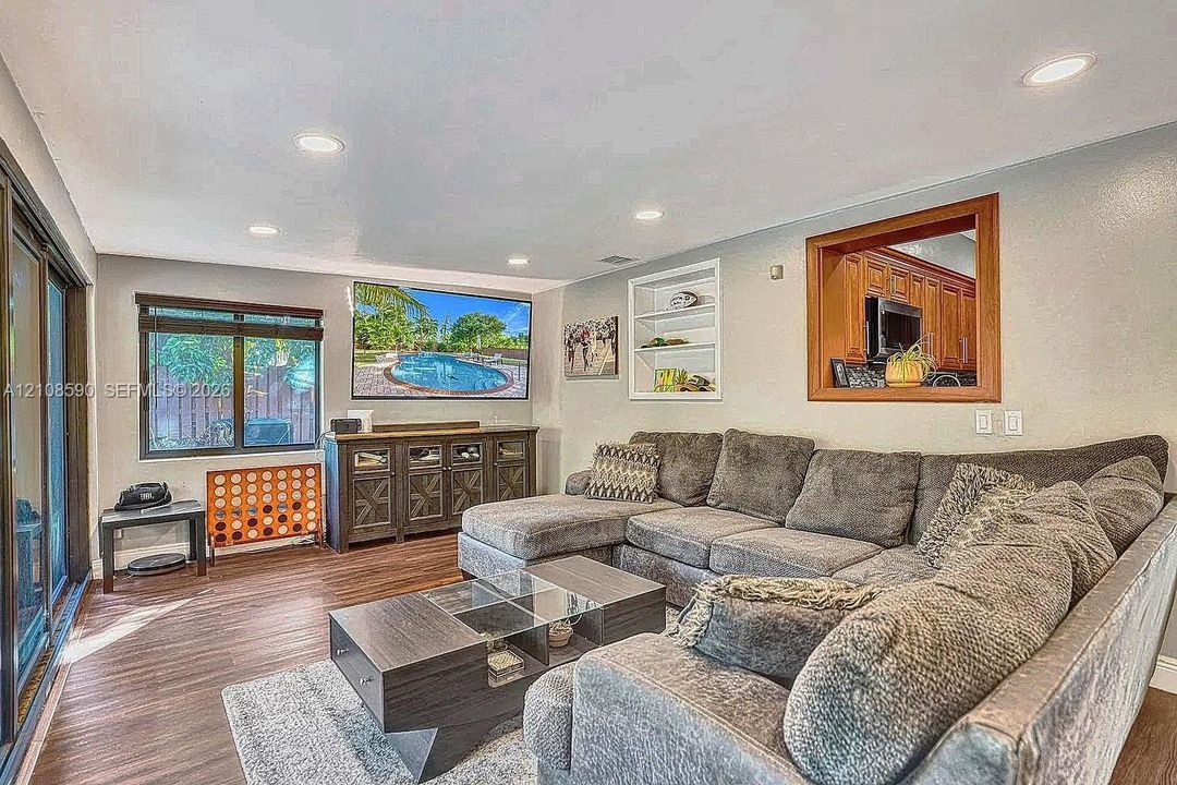 Living area featuring wood-finish flooring, recessed lighting, built-in wall shelving, and a wood-framed interior window