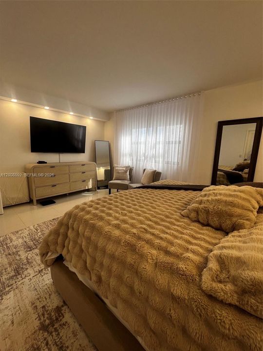 Recessed lighting, light-toned tile flooring, and a window treatment spanning the width of the wall