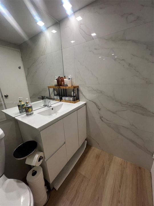 White vanity with integrated rectangular sink and polished chrome faucet, large-format veined wall tile, wood-finish flooring, and wall-to-wall mirror