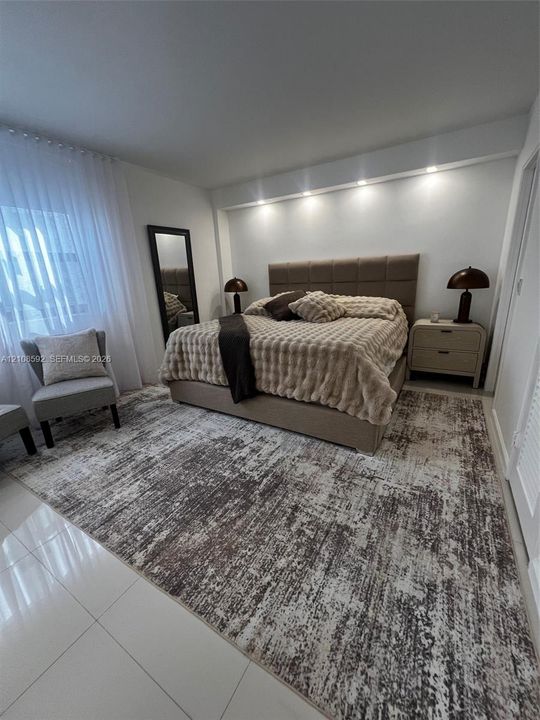 Bedroom featuring white tile flooring, neutral wall-to-wall carpeting, recessed architectural ceiling lighting, and floor-to-ceiling sheer window treatments