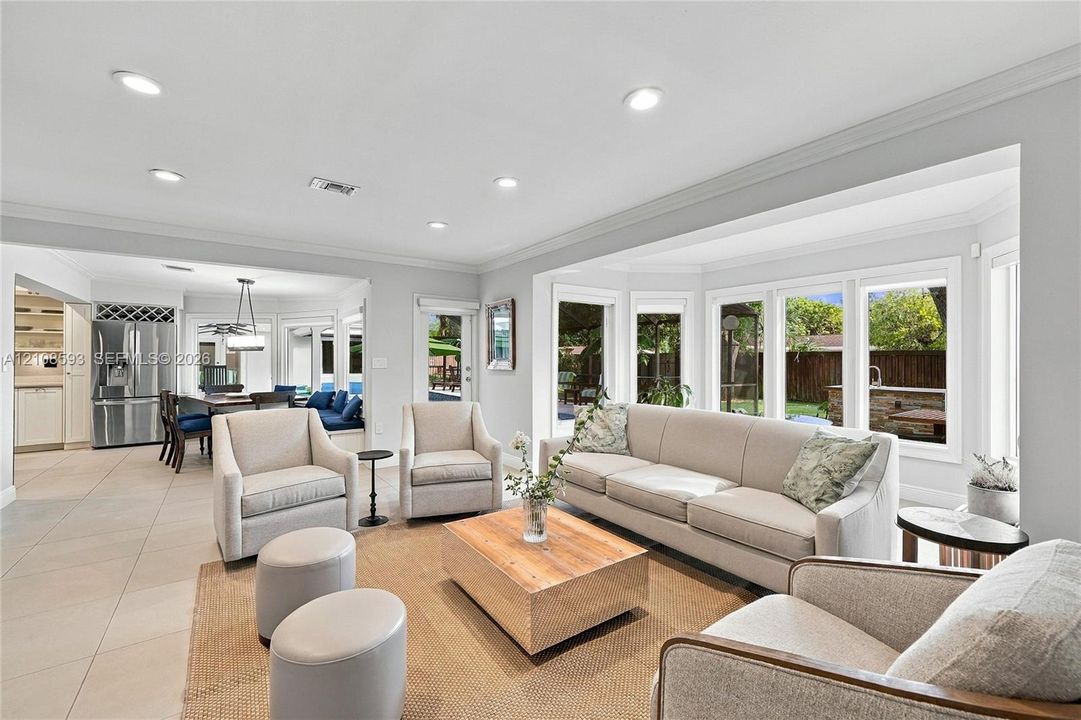 Open-concept space featuring oversized bay windows, neutral tile flooring, recessed lighting, and crown molding