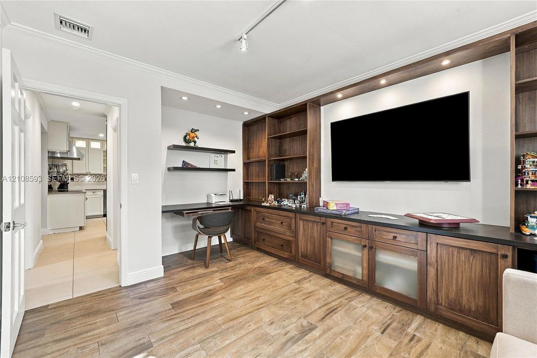 Custom built-in wood cabinetry with integrated shelving and drawers, dark countertop, recessed lighting, and wood-finish flooring