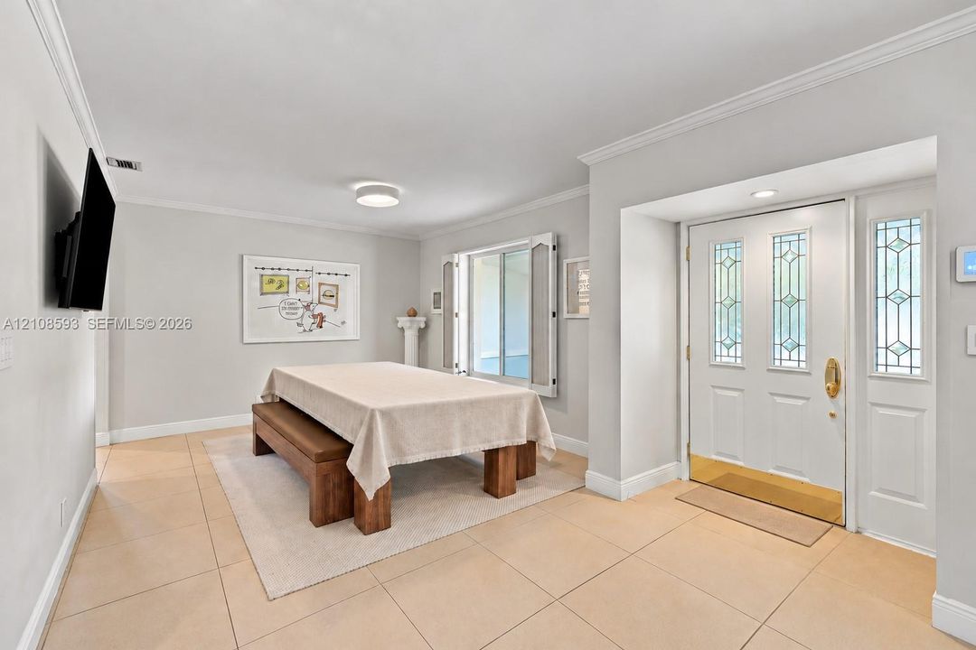 Entryway featuring neutral-tone tile flooring, crown molding, and a white front door with decorative glass inserts, brass hardware, and a matching sidelight
