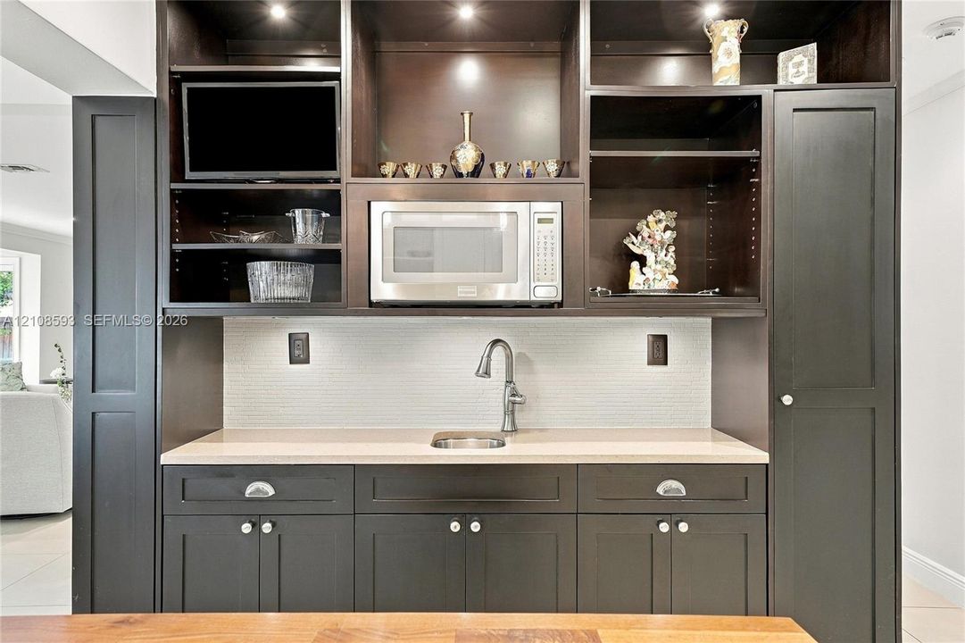 Built-in cabinetry featuring dark finish, recessed task lighting, integrated microwave, stone-finish countertop, and undermount stainless steel sink with gooseneck faucet