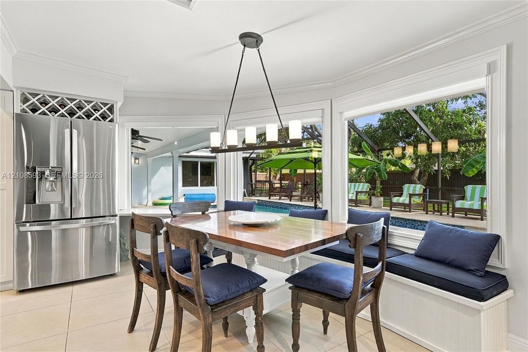 Dining area featuring large-format tile flooring, built-in window seating with integrated storage, stainless steel refrigerator with overhead wine rack, and a linear pendant light fixture
