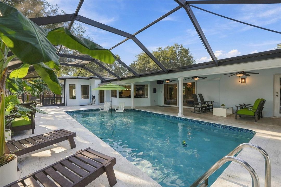 Screen-enclosed swimming pool featuring a tiled waterline, stone-finish decking, and recessed ceiling fans