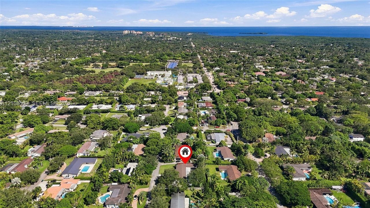 Aerial perspective of a residential property situated in a coastal region with extensive tree canopy and proximity to the waterfront