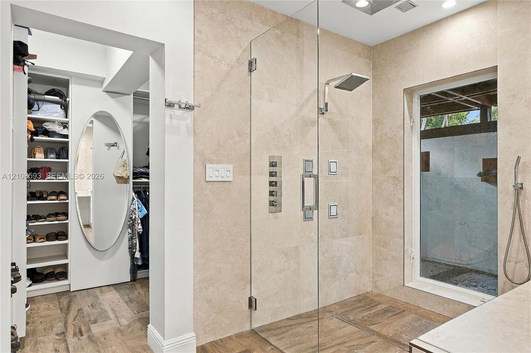 Walk-in shower featuring floor-to-ceiling stone tile, a glass enclosure, a rainfall showerhead, and a wall-mounted hand shower, paired with a built-in closet system