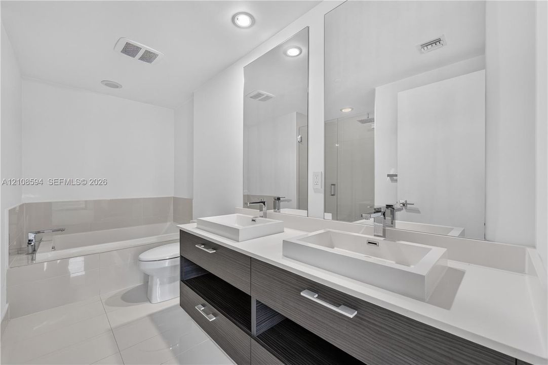 Modern floating vanity featuring dual rectangular vessel sinks, a solid surface countertop, wood-finish cabinetry, and polished chrome fixtures, complemented by floor-to-ceiling mirrors and a deep soaking tub