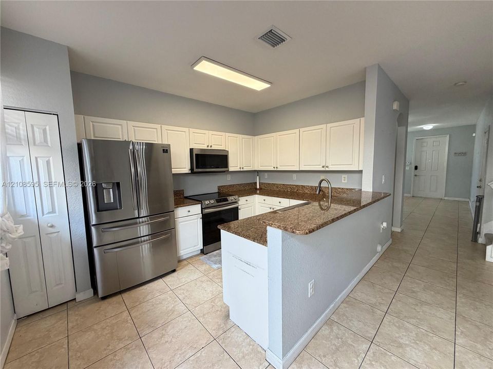 Kitchen featuring white cabinetry, stone-surface countertops, stainless steel appliances, and tile flooring