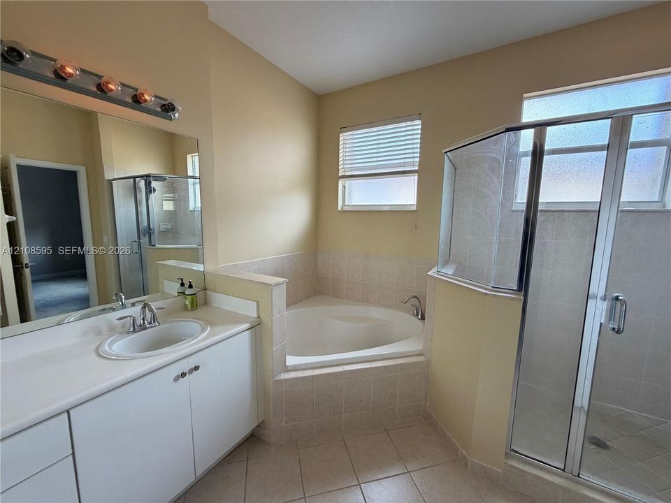 Bathroom featuring a white vanity with a solid-surface countertop, an oval-shaped soaking tub with tile surround, and a glass-enclosed shower with tiled flooring