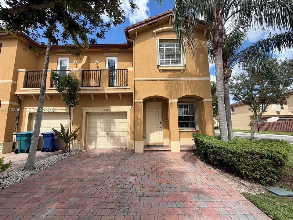 Stucco exterior featuring a paved driveway, tile roof, second-story balcony with metal railings, and arched entryway