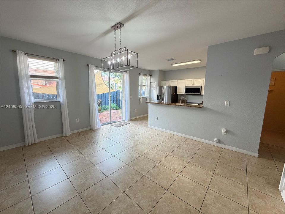 Open-concept interior featuring large-format ceramic tile flooring, a geometric metal chandelier, white kitchen cabinetry, and a sliding glass door providing exterior access