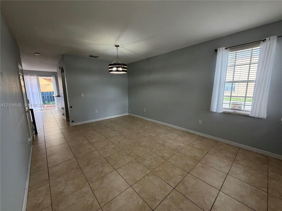 Open-concept room featuring neutral-toned tile flooring, recessed lighting, a modern drum-style pendant light, and a double-hung window