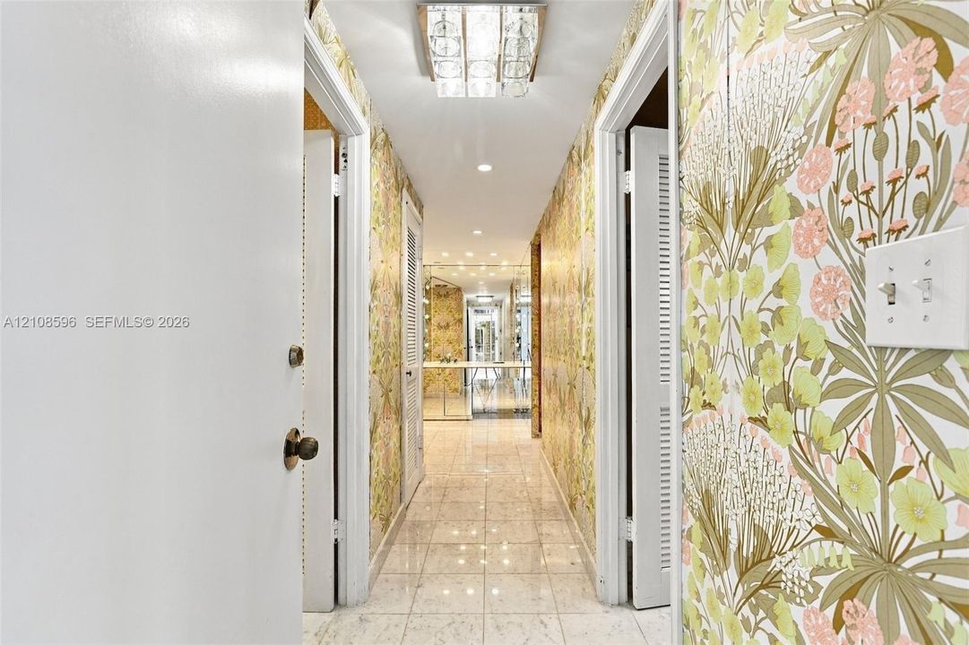 Interior hallway featuring polished stone tile flooring, botanical-patterned wallpaper, and a multi-tiered flush-mount crystal ceiling light