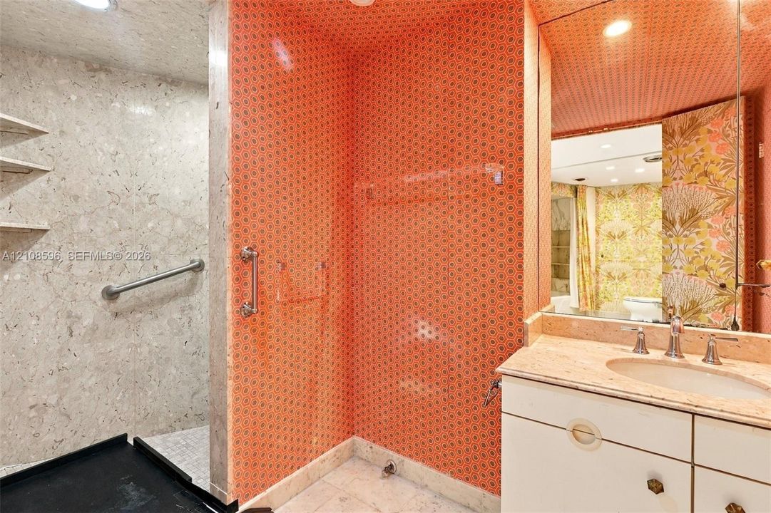 Bathroom featuring a stone-finish walk-in shower with integrated grab bar, vanity with stone countertop and undermount sink, recessed lighting, and expansive wall-to-wall mirror