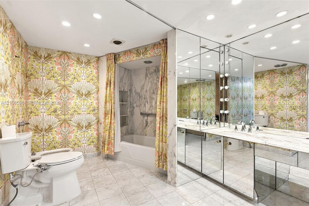 Bathroom featuring stone tile flooring, a tub-shower combination with full-height stone surround, an expansive mirrored wall, a stone vanity countertop, and recessed ceiling lighting