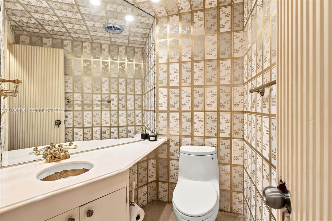 Custom vanity featuring a solid-surface countertop with an integrated oval basin and metallic-finish hardware, complemented by patterned wall-to-ceiling surfacing, a large wall-mounted mirror, and a one-piece toilet