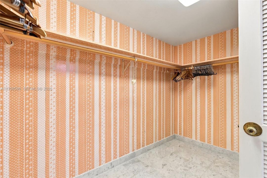 Storage space featuring built-in wooden shelving, patterned wall covering, and stone-finish flooring
