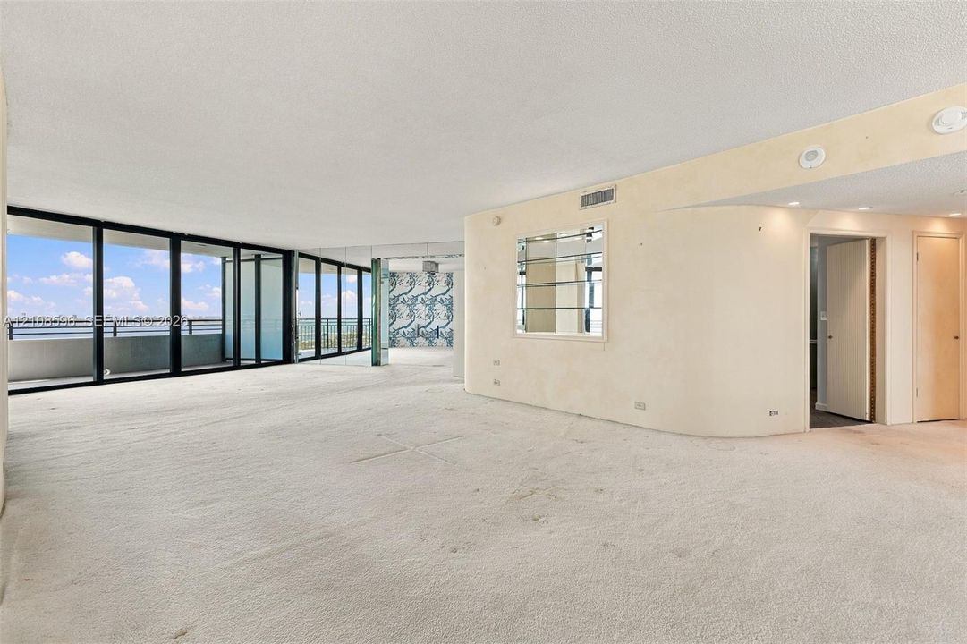 Open-concept living space featuring floor-to-ceiling windows, a curved architectural wall, recessed lighting, and a built-in recessed display niche with glass shelving