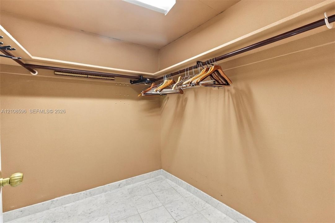 Storage space featuring dual-level hanging rods, built-in shelving, a ceiling-mounted light fixture, and stone-finish flooring