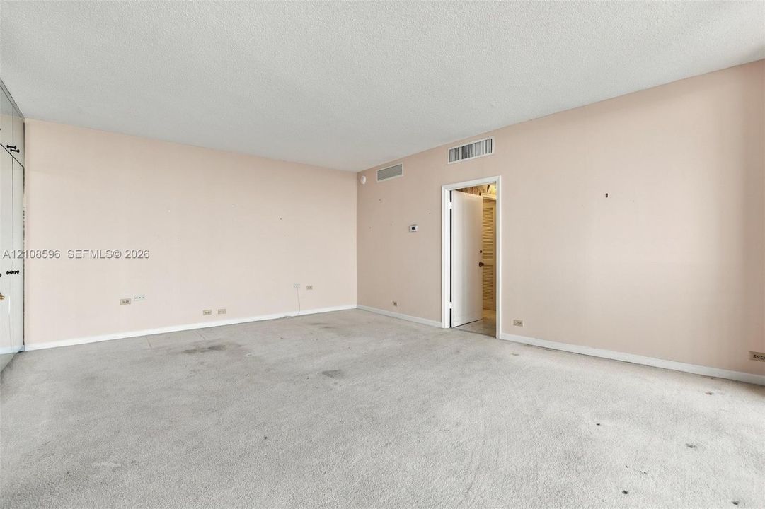 Neutral-toned interior space featuring built-in floor-to-ceiling closets, wall-to-wall carpeting, and a single-panel interior door