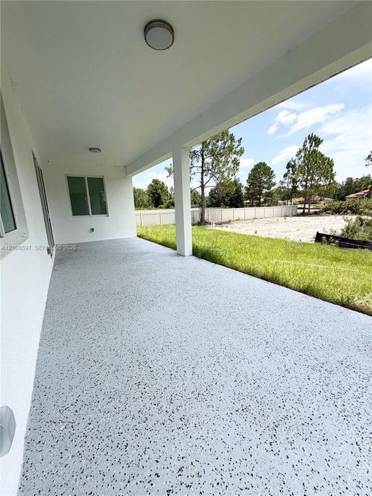 Covered concrete patio featuring a speckled epoxy finish, flush-mount ceiling lighting, and support columns
