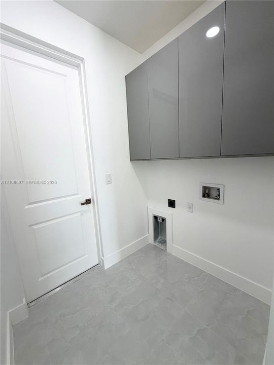 Grey high-gloss wall-mounted cabinetry, large-format tiled flooring, and a solid-core paneled door with matte black hardware