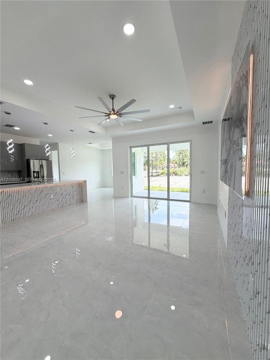Open-concept area featuring polished stone-finish flooring, recessed lighting, a coffered ceiling with a modern multi-blade ceiling fan, and a kitchen island with stone-finish cladding