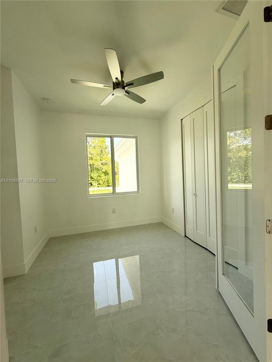 Room featuring polished tile flooring, a multi-blade ceiling fan, white bi-fold closet doors, and a glass-paneled entry door