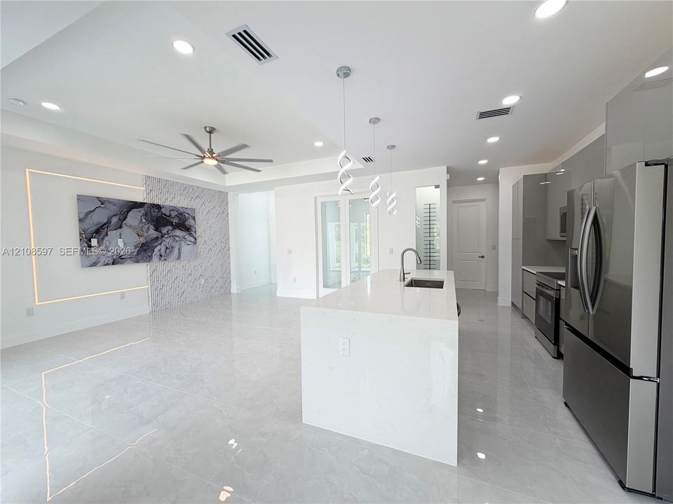 Open-concept kitchen featuring an expansive quartz-topped island, high-gloss cabinetry, stainless steel appliances, recessed lighting, and a stone-accented wall with integrated perimeter lighting