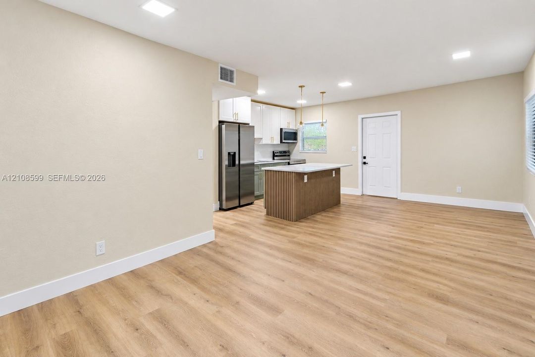 Open-concept kitchen featuring wood-finish flooring, a central island with a countertop, stainless steel refrigerator, white cabinetry, and recessed lighting