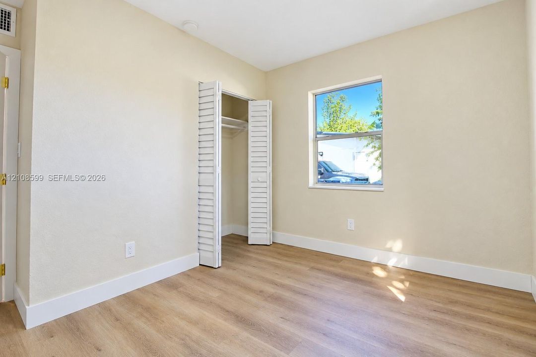 Neutral-toned room featuring wood-finish flooring, a single-hung window, and a built-in closet with louvered bi-fold doors