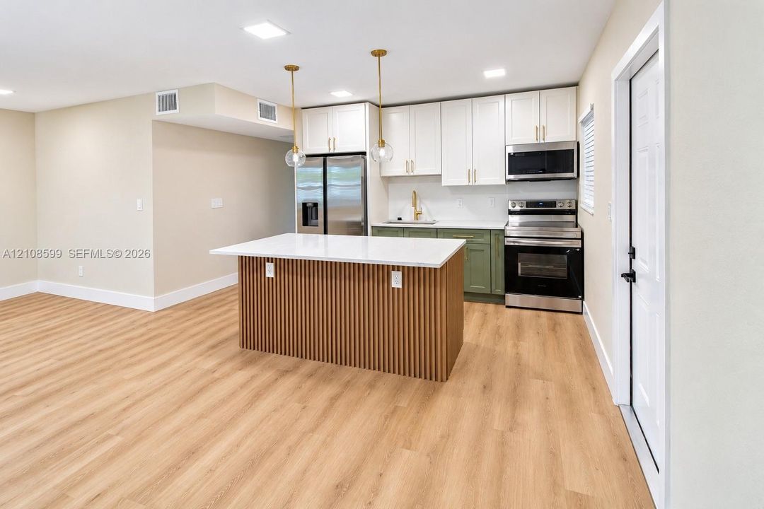Kitchen featuring a center island with slatted wood detailing and a solid-surface countertop, two-toned shaker-style cabinetry, stainless steel appliances, and wood-finish flooring