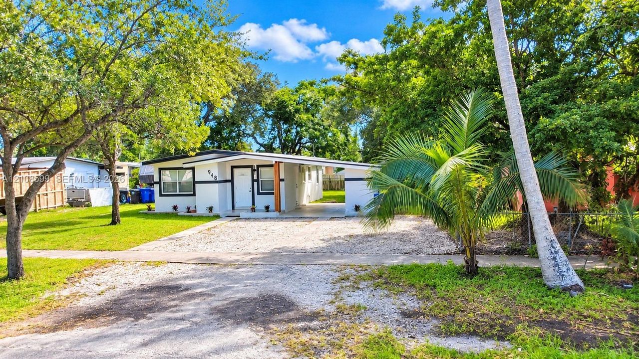 Single-story exterior featuring white stucco siding, contrasting trim, an integrated carport, and mature landscaping