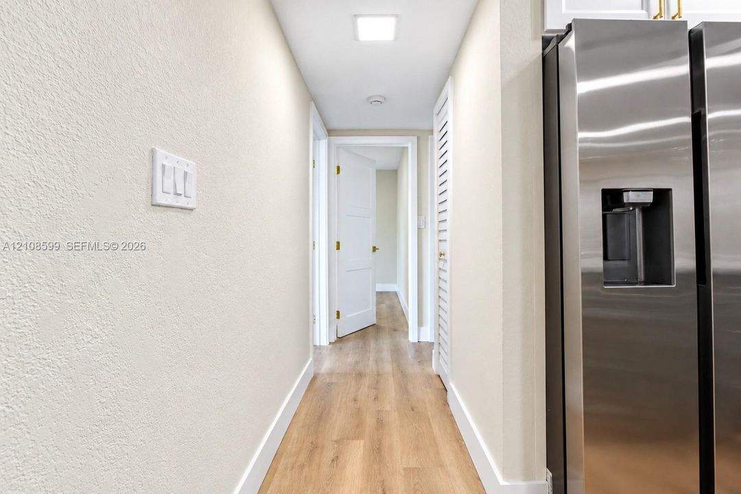 Stainless steel refrigerator, wood-finish flooring, white panel doors, and louvered closet doors