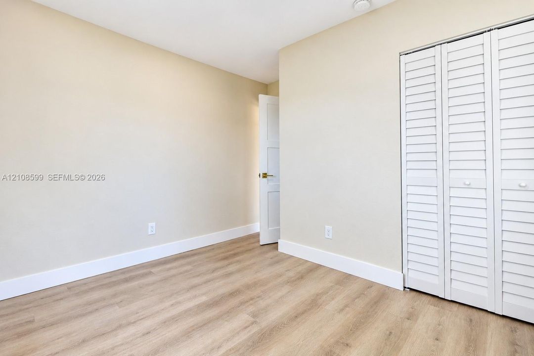 Interior room featuring wood-finish flooring, white louvered closet doors, and neutral wall paint