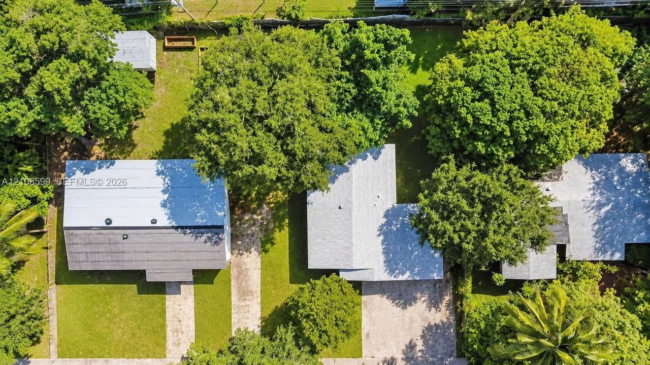 Aerial view of the property featuring a manicured lawn, established mature trees, a detached storage structure, and paved driveways