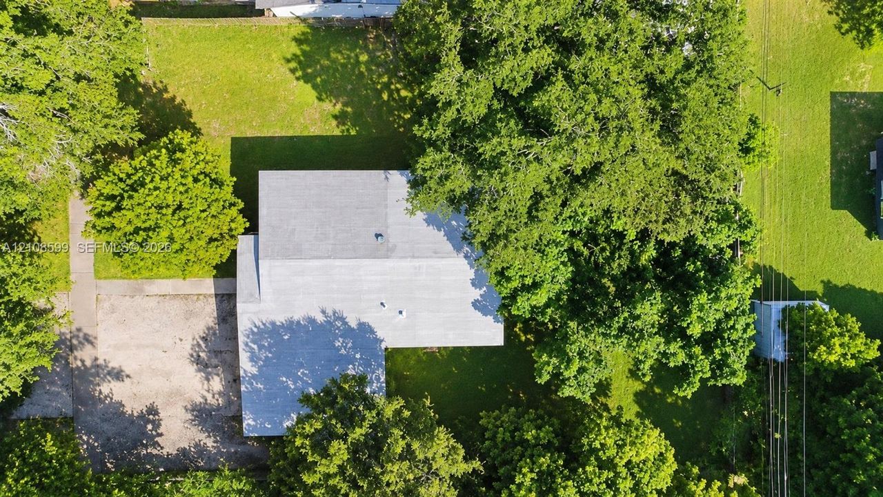Aerial perspective featuring a spacious lot with mature trees and a concrete driveway
