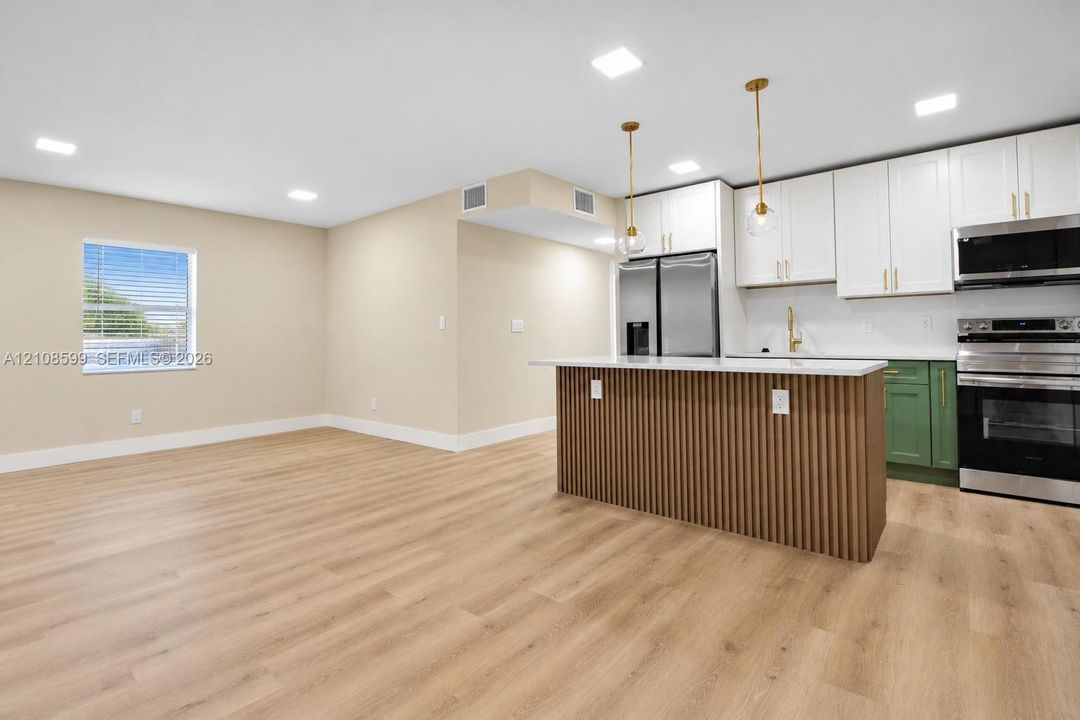 Kitchen featuring a slatted wood-finish island, white and green cabinetry, stainless steel appliances, and wood-finish flooring