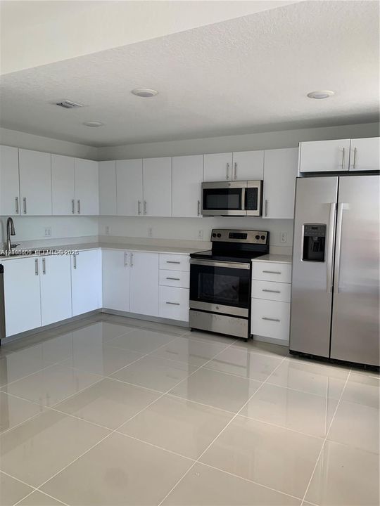 Kitchen featuring white cabinetry, solid-surface countertops, large-format tile flooring, and stainless steel appliances including a built-in microwave and refrigerator