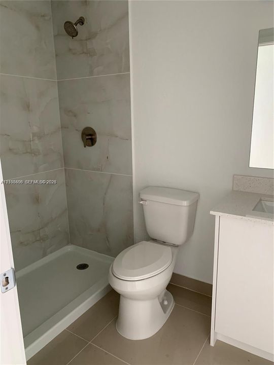 Bathroom featuring a walk-in shower with large-format wall tile, metallic finish shower fixtures, a vanity with a stone-composite countertop, and ceramic tile flooring