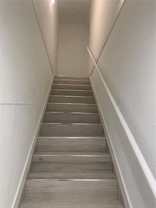Staircase featuring wood-finish treads, metal nosing, and a continuous white wall-mounted handrail